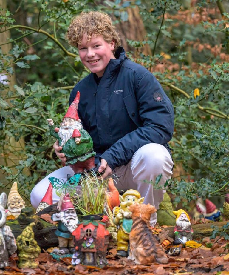 -Joris-Jan- Een jongen poseert tussen kleurrijke tuinkabouters in een bosrijke omgeving.